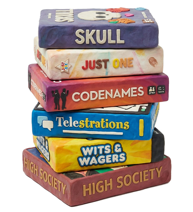 A stack of board game boxes modelled in plasticine: Skull, Just One, Codenames, Telestrations, Wits & Wagers and High Society.